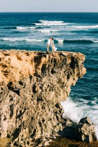 bride and groom on cliff over the ocean in Hawaii