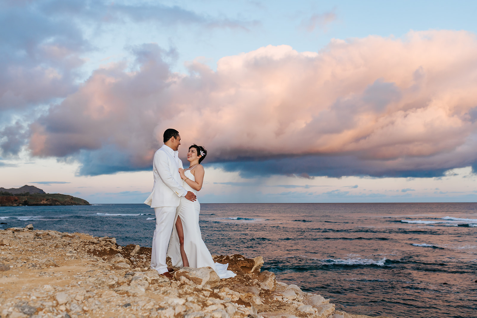 Bride and Groom on Kauai beach with pink clouds and the ocean in the background.