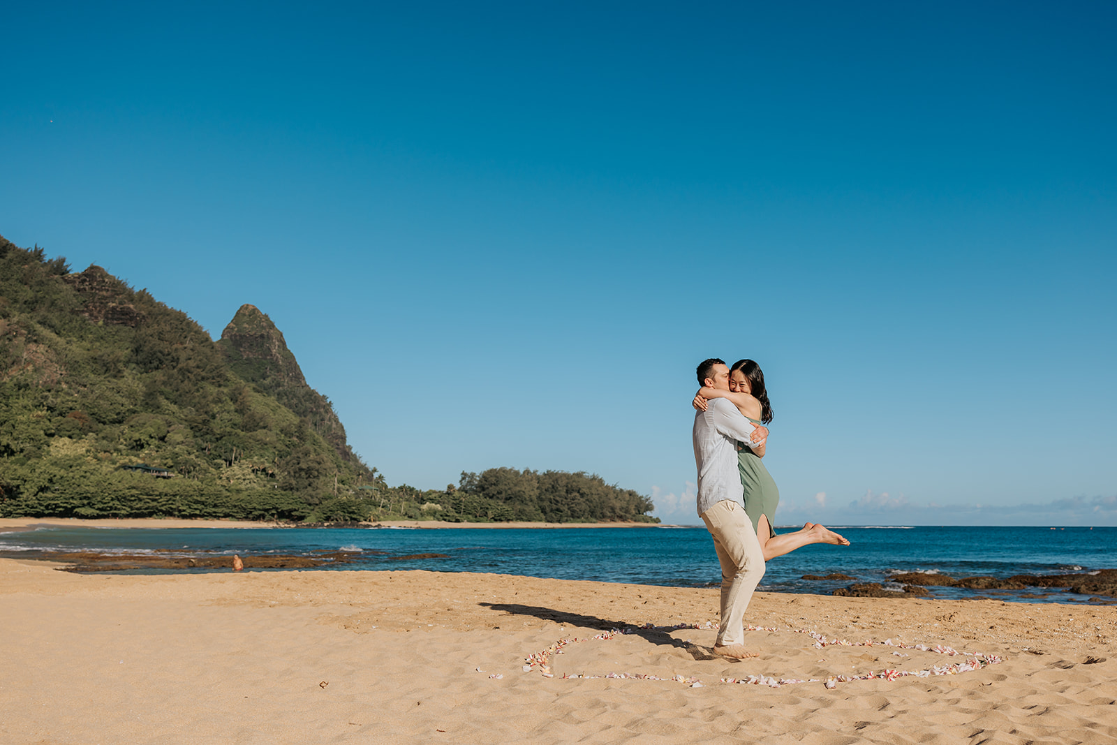 Couple at Tunnels beach on Kauai, he is picking her up and they are smiling.